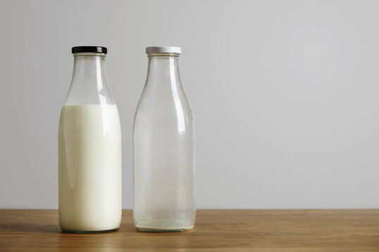 Volle und leere Milchflasche auf hölzerner Oberfläche stehend.