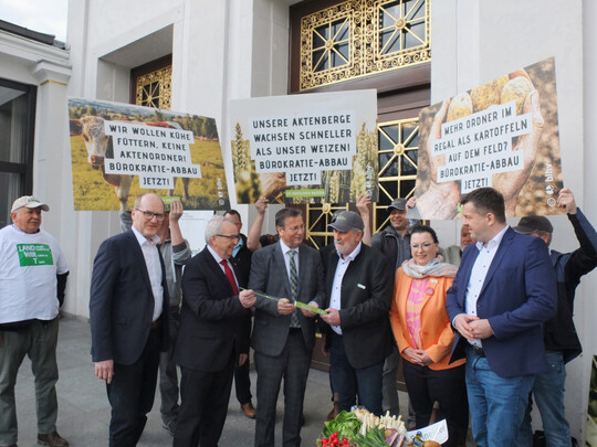 Übergabe des Zollstocks (v. l.): Hans-Benno Wichert, Vizepräsident im Landesbauernverband Baden-Württemberg; Till Backhaus, Agrarminister Mecklenburg-Vorpommern; Peter Hauk, Landwirtschaftsminister Baden-Württemberg; Bernhard Bolkart, Präsident im Badischen Landwirtschaftlichen Hauptverband; Christiane Wangler, Präsidentin LandFrauenverband Südbaden und Sven Schulze, Landwirtschaftsminister Sachsen-Anhalt, umrahmt von protestierenden Landwirten.