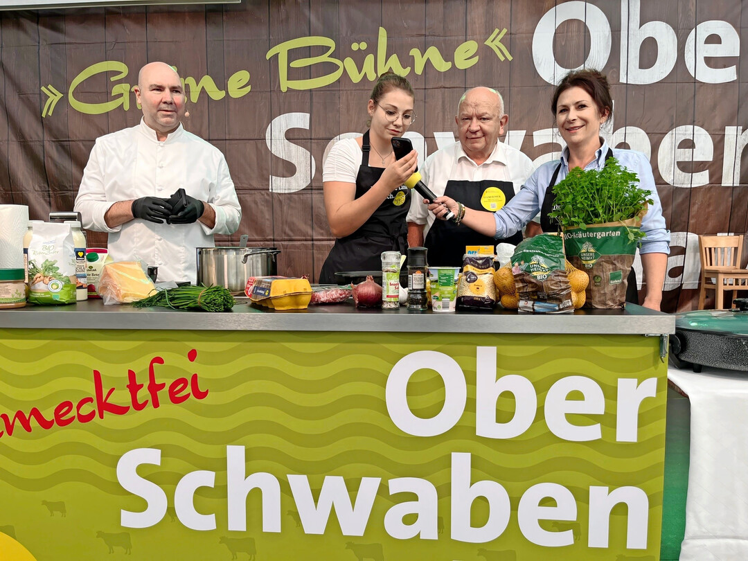 Beim gro�en Kochduell mit Showkoch Eberhard Braun (links) und Andrea Gmeinder, Leiterin Landwirtschaftsamt Ravensburg (rechts), waren alle Pl�tze auf dem Gr�nen Pfad voll besetzt. Gekocht wurde ein von ChatGPT vorgeschlagenes, einfaches Gericht aus Speck und Linsen, das Kochpartnerin Ramona Kreuzer (Mitte) zu Beginn der Veranstaltung mit dem Handy �bers Internet abrief. Als vierter Kochpartner sorgte der Innungsmeister des B�ckerhandwerks, Gerold Heinzelmann, f�r beste Unterhaltung.  