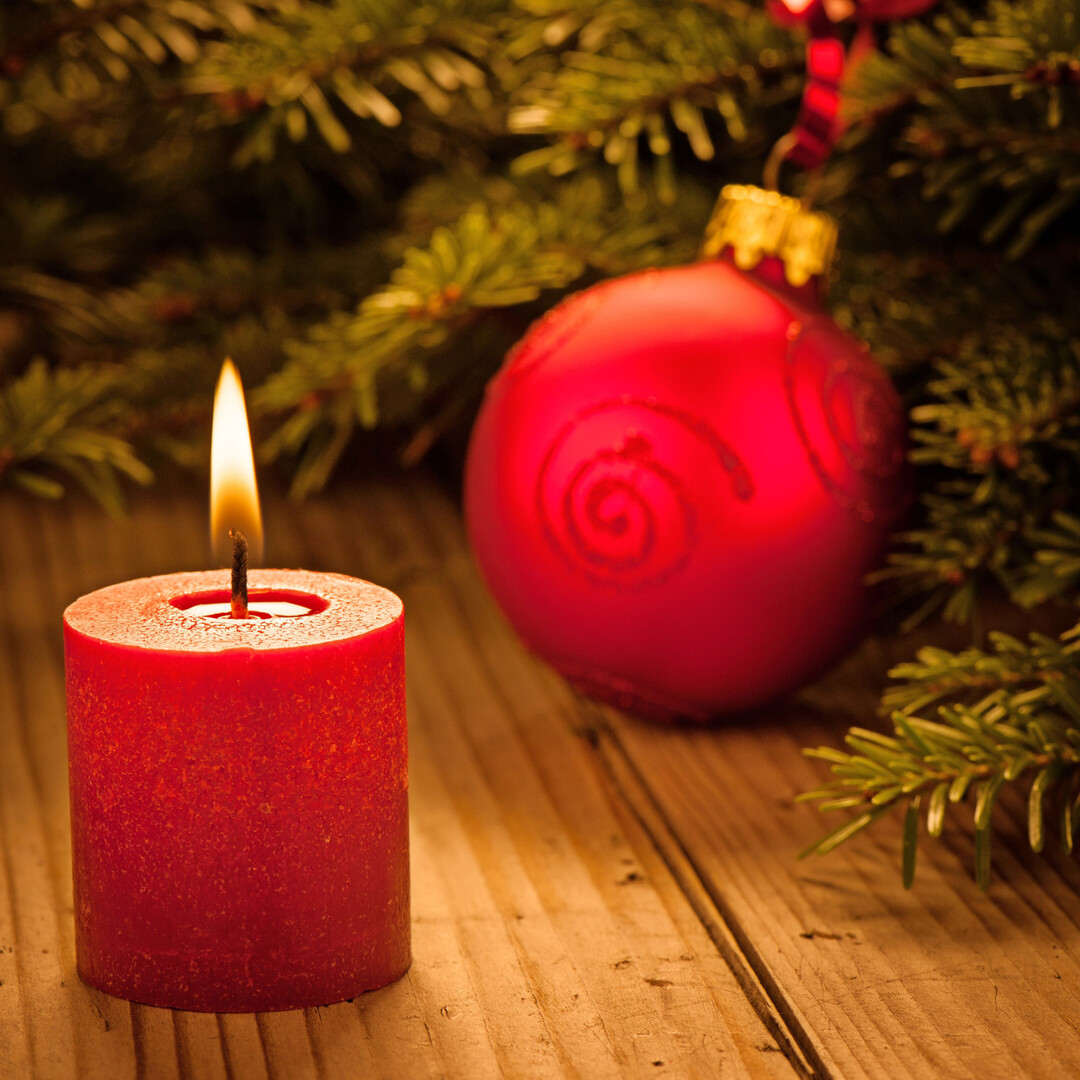 Weihnachtliche Atmosphäre mit einer roten brennenden Kerze und einer Kugel, von Tannenzweigen umgeben