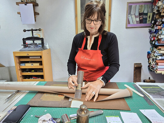 F�r die Aufarbeitung des Buchr�ckens sucht Christiane Rux eine Pappe in der passenden Farbe heraus. Links hinten ist eine Buchpresse zu sehen.