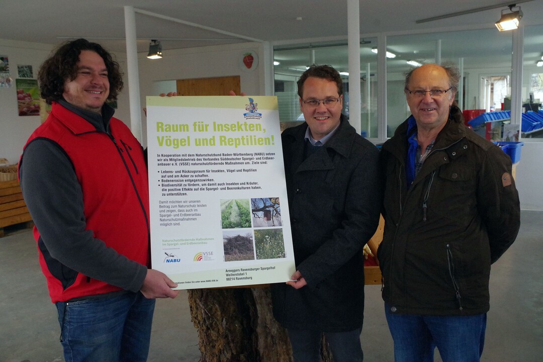 Das Schild, das die Umsetzung der durch den NABU vorgeschlagenen Maßnahmen dokumentiert, wird von Schumacher an Arnegger überreicht. Mayer von der NABU-Ortsgruppe Ravensburg (rechts) hat den Landwirt beraten.