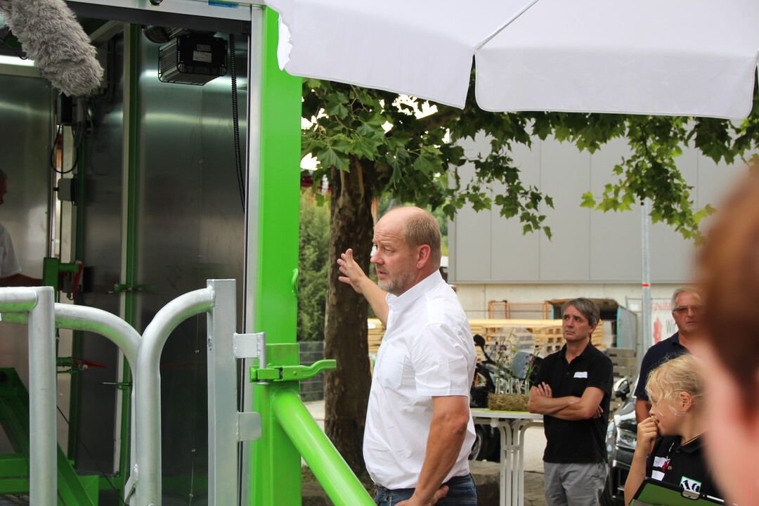 Der grüne Schlitten fährt auf Schienen aus dem Anhänger heraus, alles geht vollautomatisch und sehr geräuscharm. Das Rind muss den Schlitten betreten, um den Kopf durch die Fressfangvorrichtung stecken zu können. Thomas Mayer erklärt den Journalisten das Vorgehen direkt an der Mobilen Schlachteinheit.