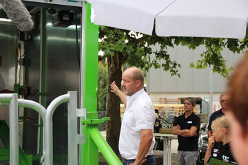 Der grüne Schlitten fährt auf Schienen aus dem Anhänger heraus, alles geht vollautomatisch und sehr geräuscharm. Das Rind muss den Schlitten betreten, um den Kopf durch die Fressfangvorrichtung stecken zu können. Thomas Mayer erklärt den Journalisten das Vorgehen direkt an der Mobilen Schlachteinheit.