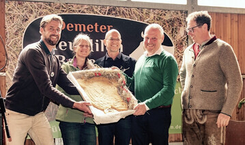 V.l.n.r.: Christoph Reiber (Gesch�ftsf�hrer Demeter Baden-W�rttemberg), Ute Haimerl (Gesch�ftsf�hrerin Demeter Bayern) und Alexander Gerber (Vorstand Demeter e.V.) �berreichen Rolf Holzapfel und Andreas Aufmuth (beide Vorst�nde bei den Demeter HeuMilch Bauern) auf der Jubil�umsfeier in Ankenreute einen gro�en Keks in Form einer Kuh � gebacken von Demeter-B�ckermeisterin Anne Dorer von der Eselsm�hle.